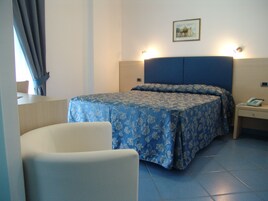 A hotel room with a bed, a chair, a bedside table with a phone, and a picture on the wall.