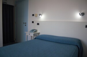 Una habitación de hotel con cama, mesita de noche y teléfono, además de una puerta.