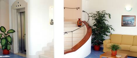 Un espacio habitable amplio con una escalera curva, un sofá, una mesa de centro y plantas en macetas.