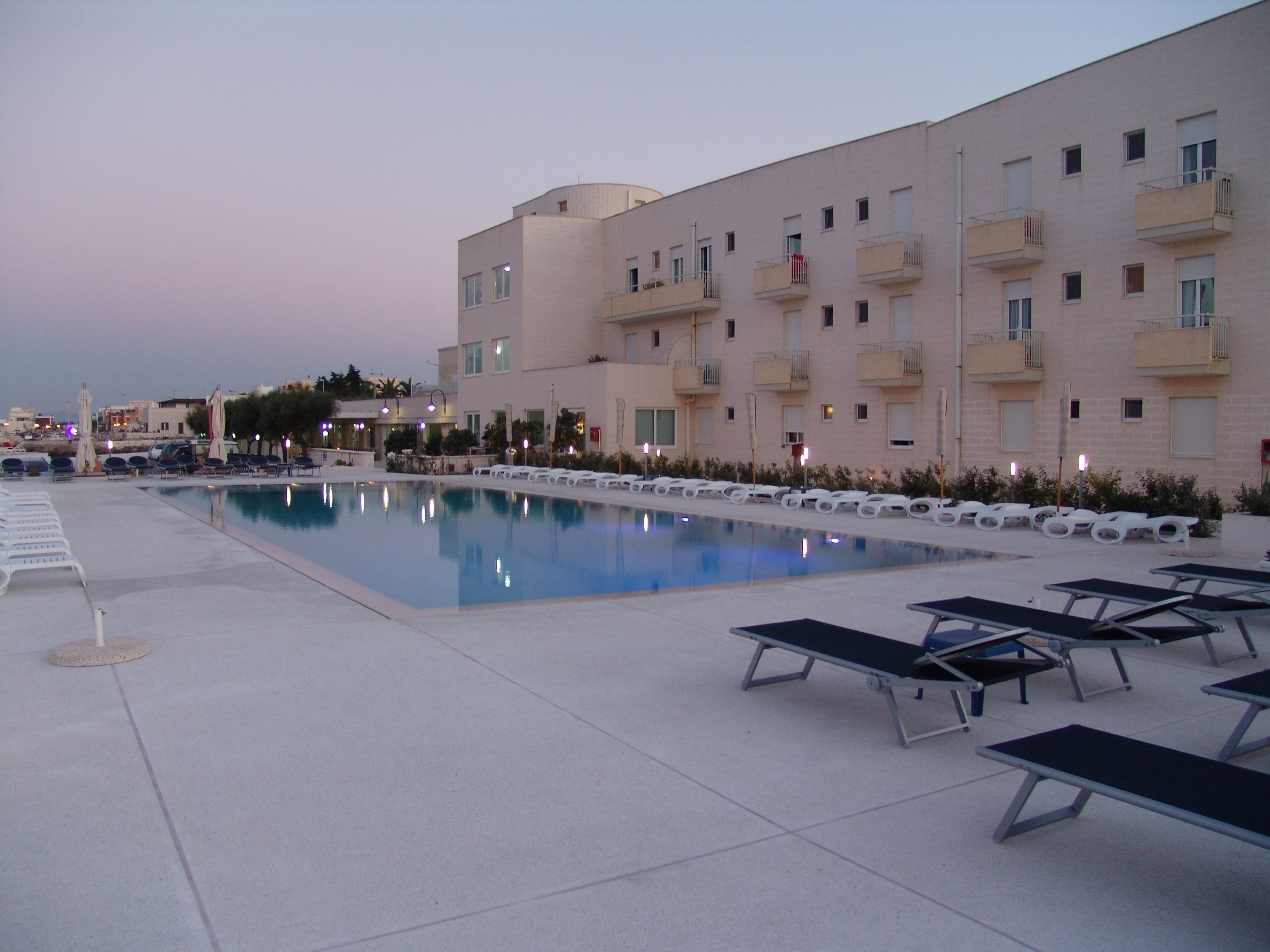 Una piscina con sillones de descanso y un edificio con balcones al fondo.