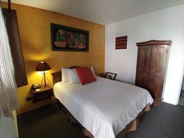Habitación de hotel con cama, mesita de noche con l ámpara, armario de madera y un cuadro en la pared.