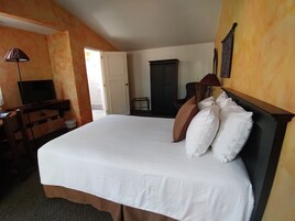 Ein Hotelzimmer mit einem großen Bett, einem Schreibtisch mit Fernseher, einem Kleiderschrank und einer Tür, die auf einen Balkon führt.