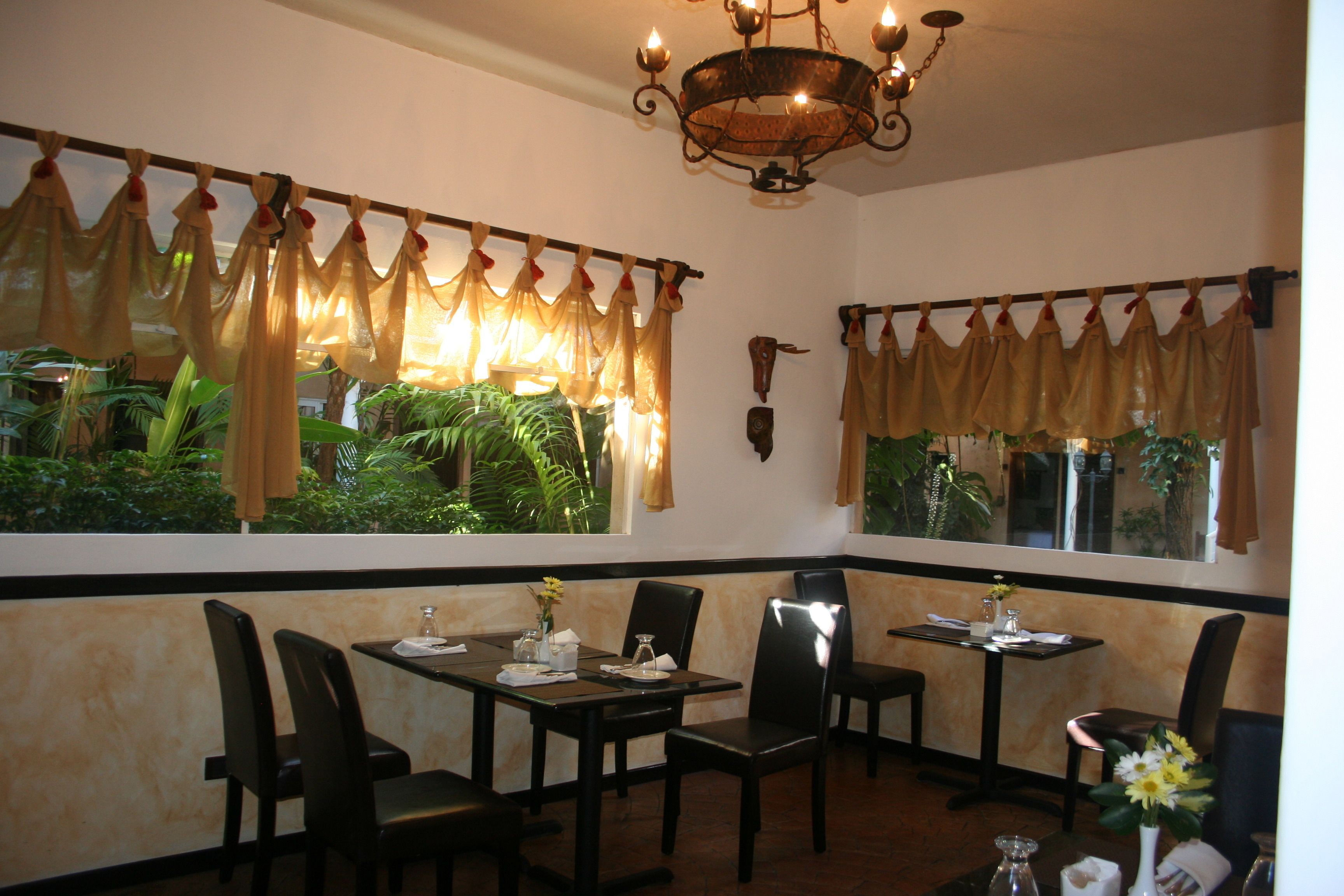 L’intérieur d’un restaurant avec deux tables, des chaises, un lustre et de grandes fenêtres ornées de rideaux.