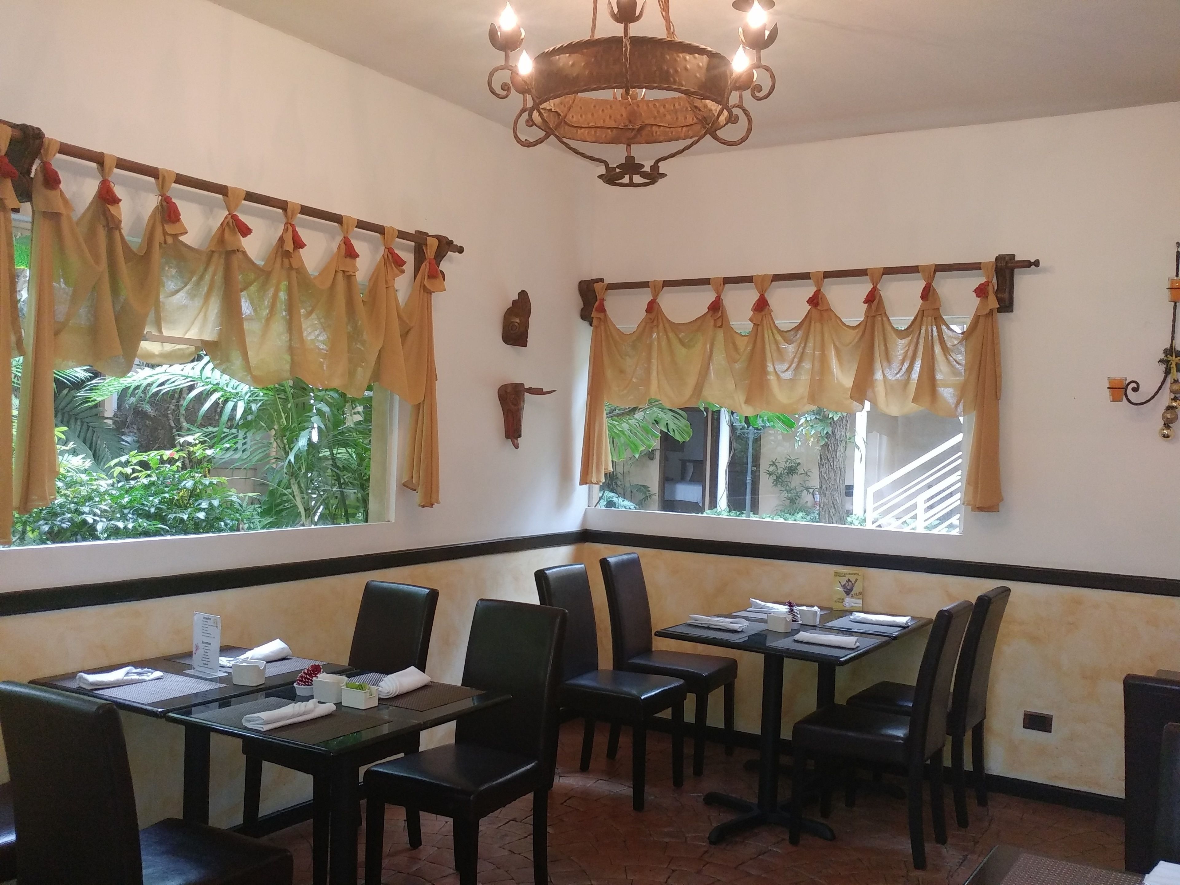 A restaurant with tables and chairs, a chandelier, and windows with curtains.