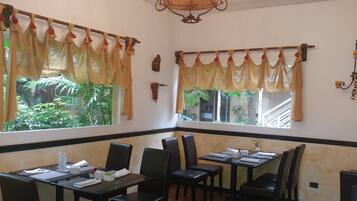 A restaurant with tables and chairs, a chandelier, and windows with curtains.