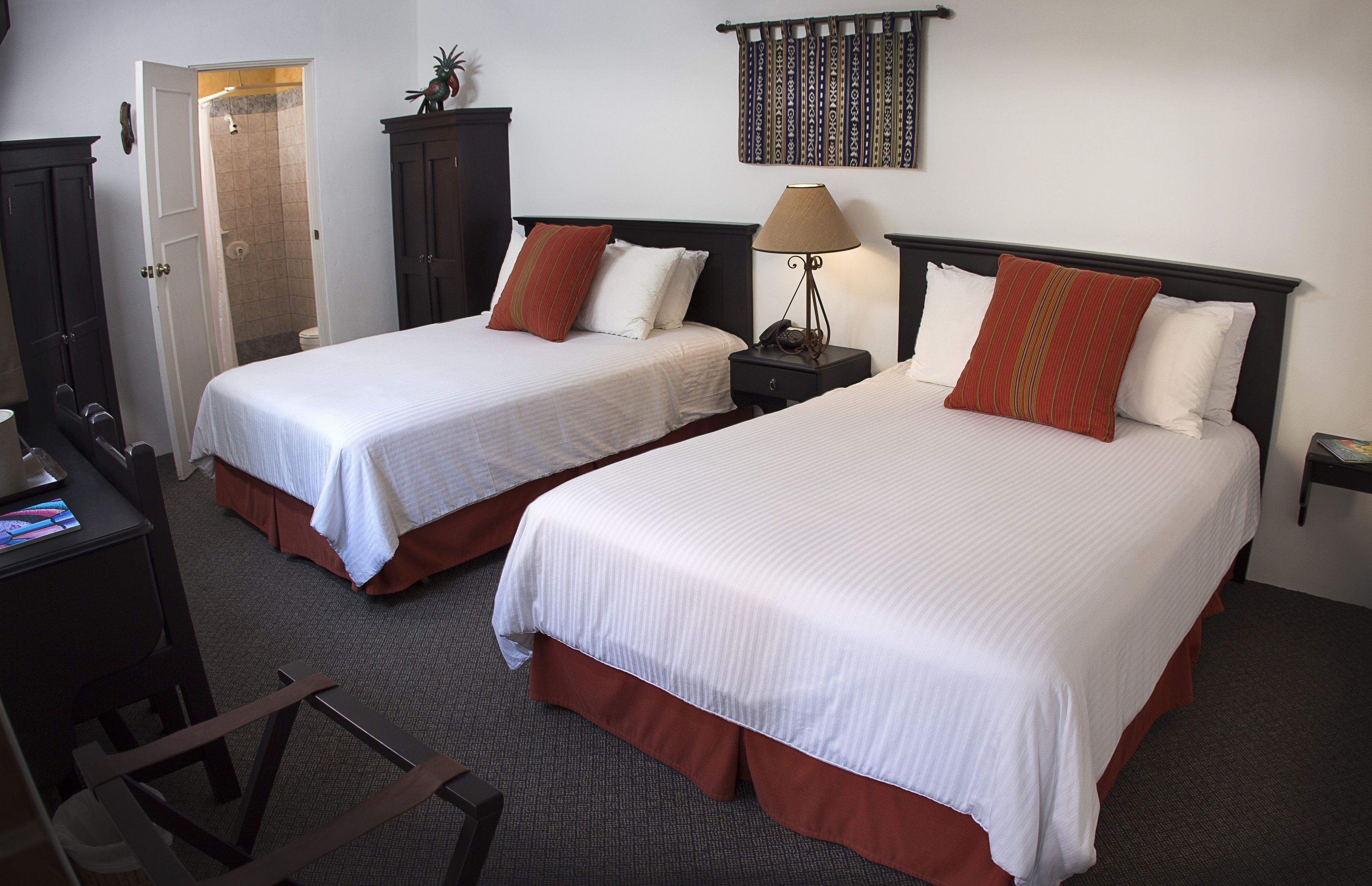 A hotel room with two beds, a desk, and a shower area.
