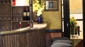 Eine Bar mit Hockern, ein Regal mit Weinflaschen, eine Vase mit Blumen und ein an der Wand montierter Fernseher.