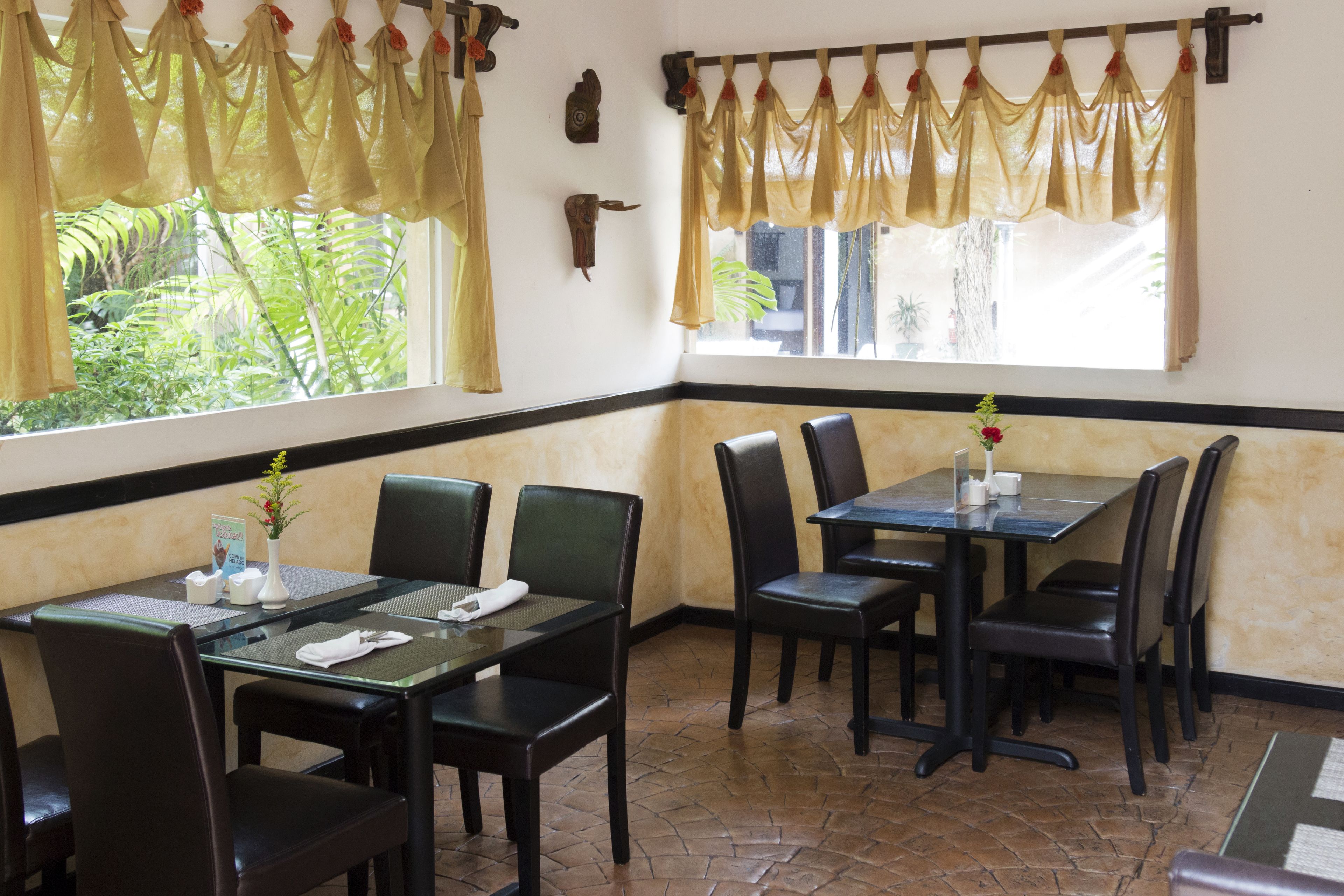 A restaurant with a corner table and chairs, a vase with flowers, and a window with curtains.