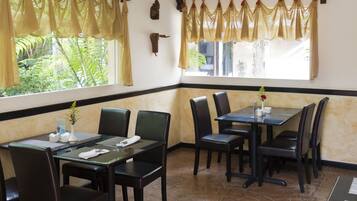 A restaurant with a corner table and chairs, a vase with flowers, and a window with curtains.