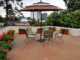 Eine Terrasse mit vier Stühlen und einem Tisch, umgeben von Topfpflanzen und einem großen Sonnenschirm.