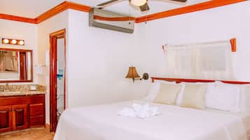Habitación de hotel con cama, tocador con espejo, ventilador de techo y ventana con cortinas.