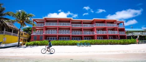 Un hotel de varios pisos con balcones, situado en una playa de aguas cristalinas.