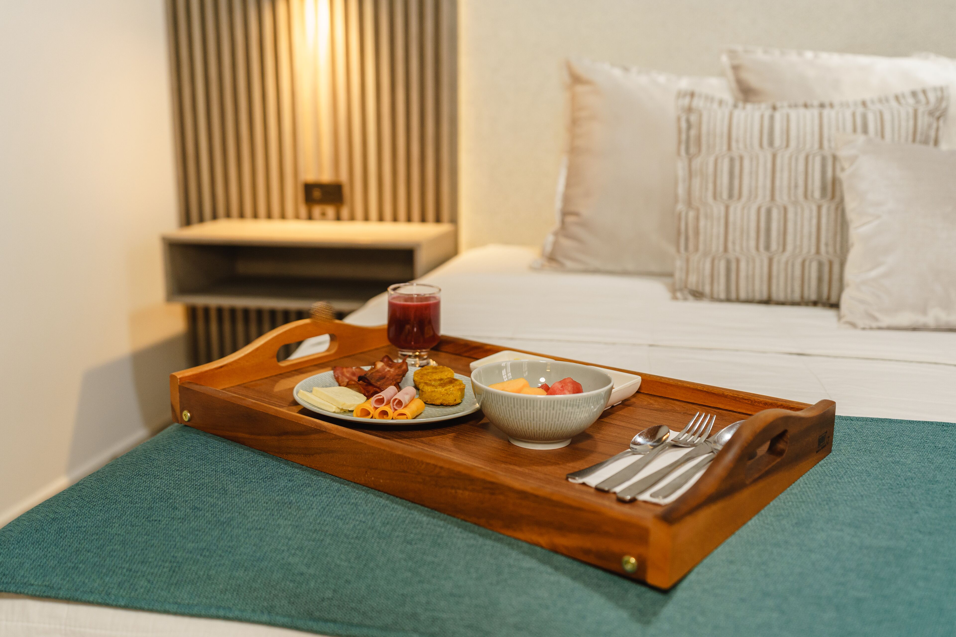 A breakfast tray with food and drinks on a wooden tray, placed on a bed with a green bedspread.