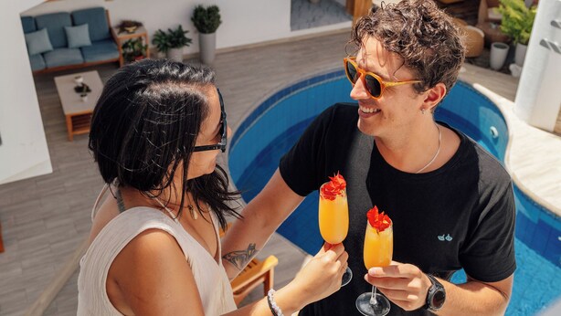 A man and a woman standing by a pool, holding drinks with fruit garnishes. - Hotel Santa Fe (Puerto Ayora)