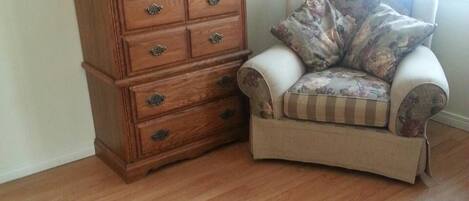 A room with a wooden dresser and a chair with floral upholstery.