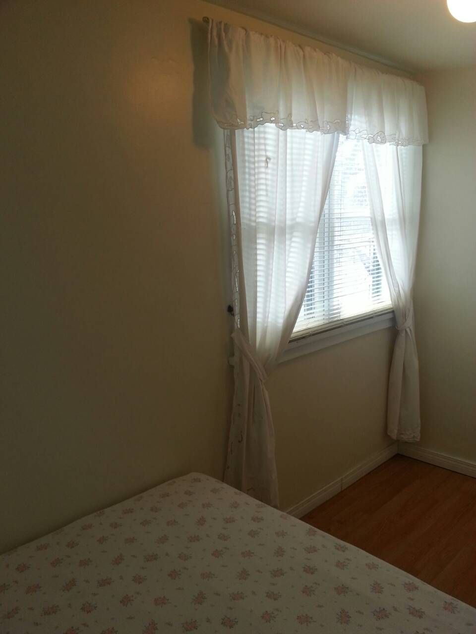 A room with a single window, a bed with floral bedding, and a plain wall.