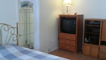 Un dormitorio con una cama, un mueble de televisión de madera, una televisión, una lámpara y un armario.