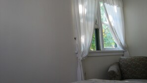 A room with a bed, a window with white curtains, and a floral-patterned chair.