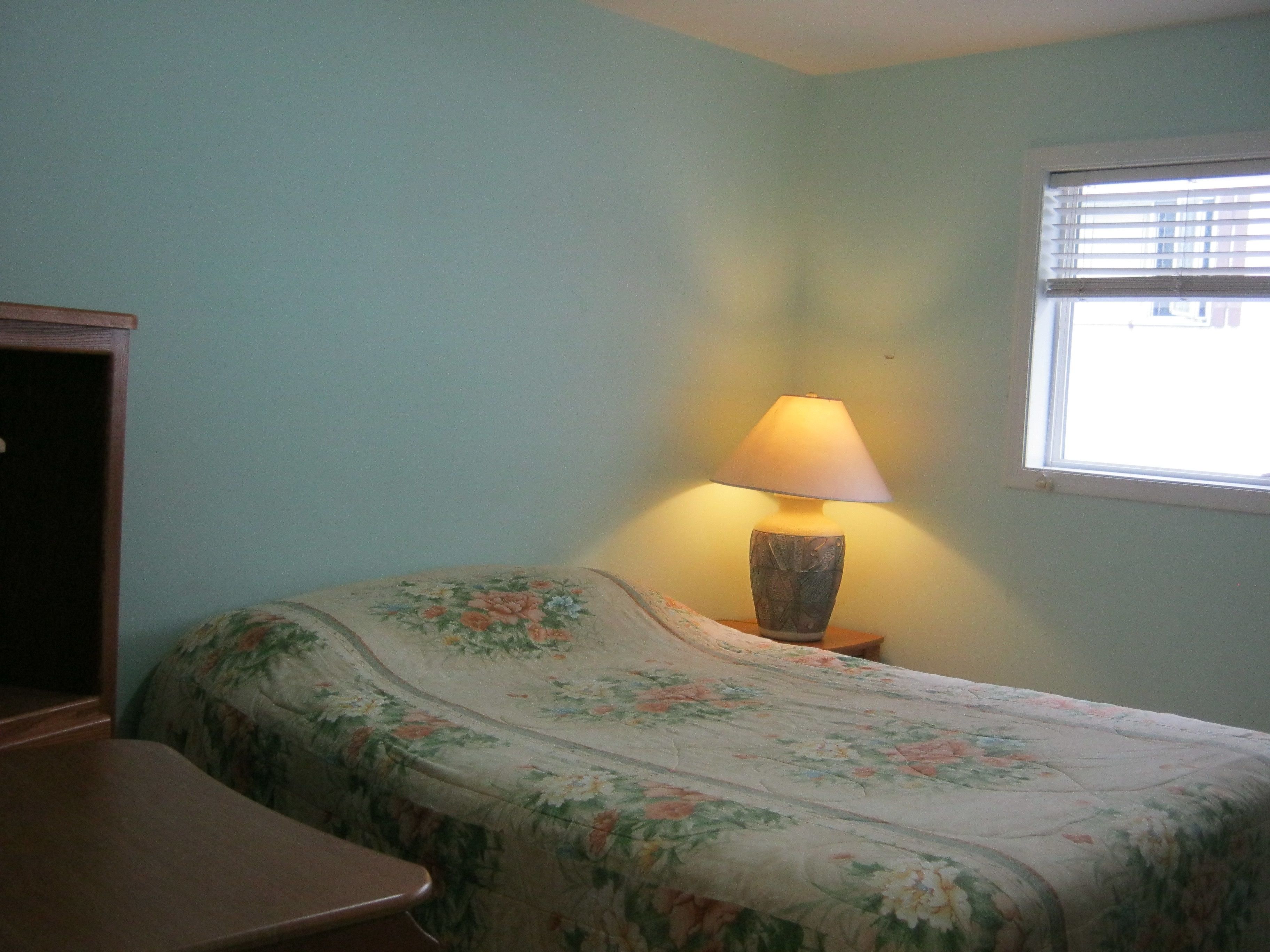A bedroom with a bed, a nightstand, a lamp, and a window.