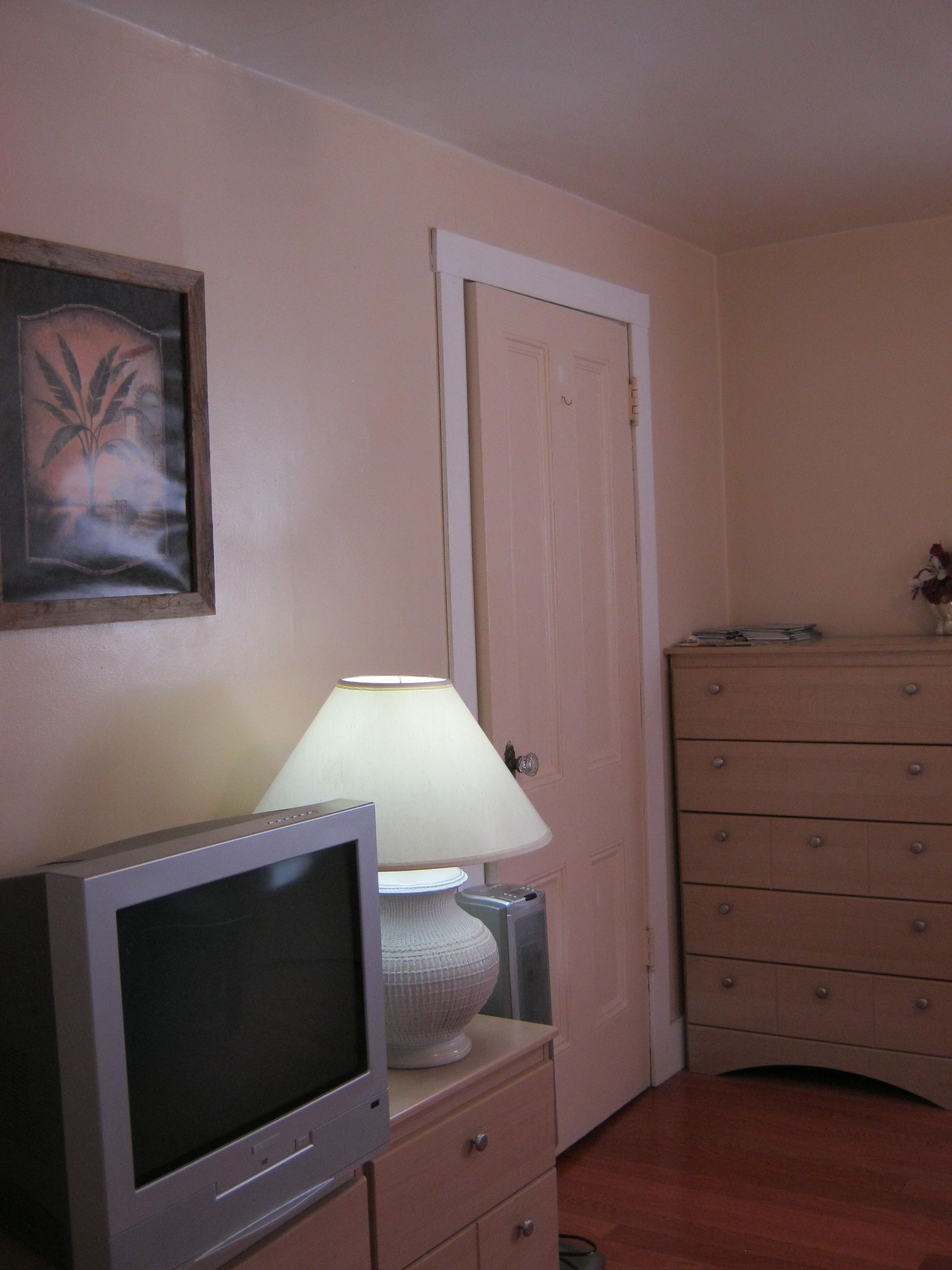 Una habitación con televisión sobre una cómoda, una lámpara, una puerta y una cómoda con cajones.