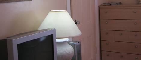 Una habitación con televisión sobre una cómoda, una lámpara, una puerta y una cómoda con cajones.
