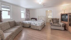 A room with a sofa, two single beds, a chair, and a television.
