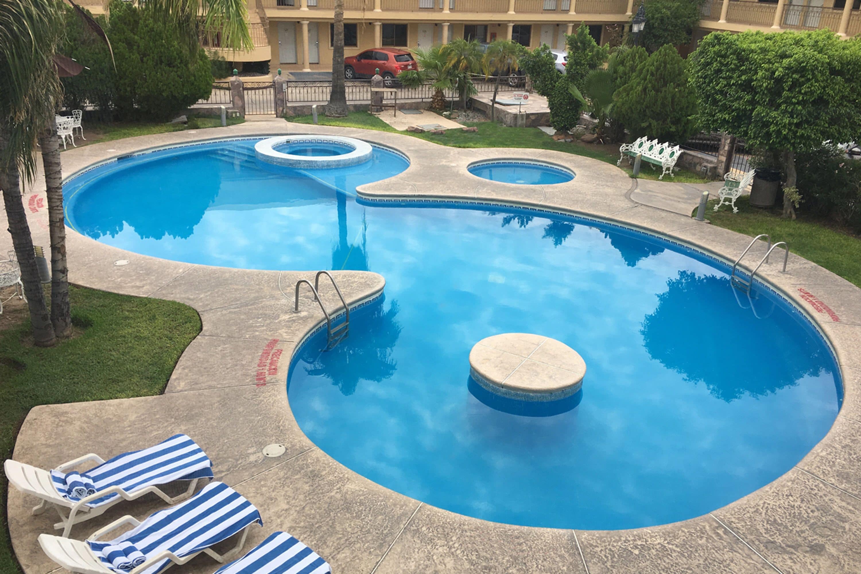 A swimming pool with three circular sections, surrounded by lounge chairs and a building in the background.