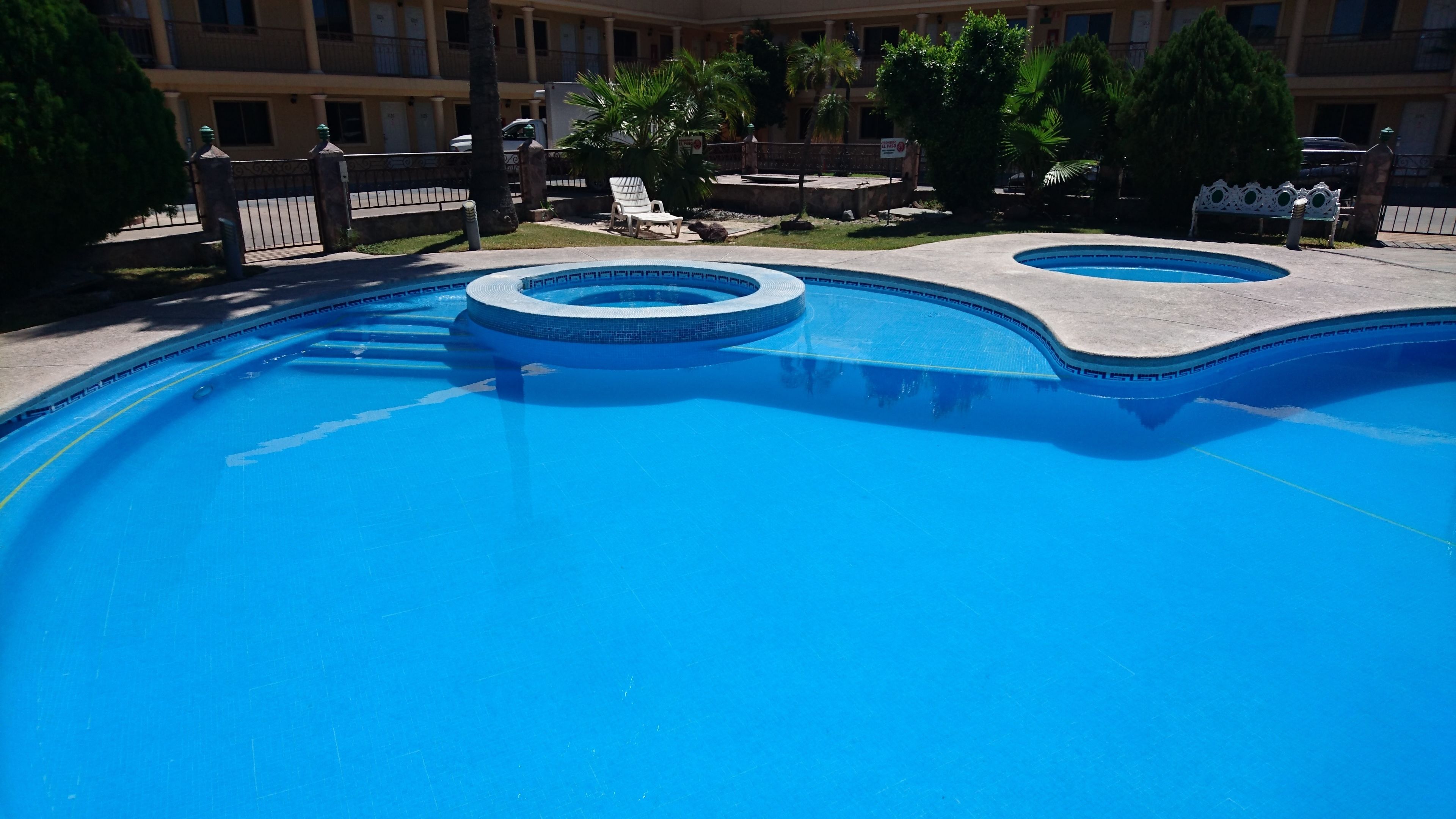 A swimming pool with two circular sections and a surrounding deck with lounge chairs.