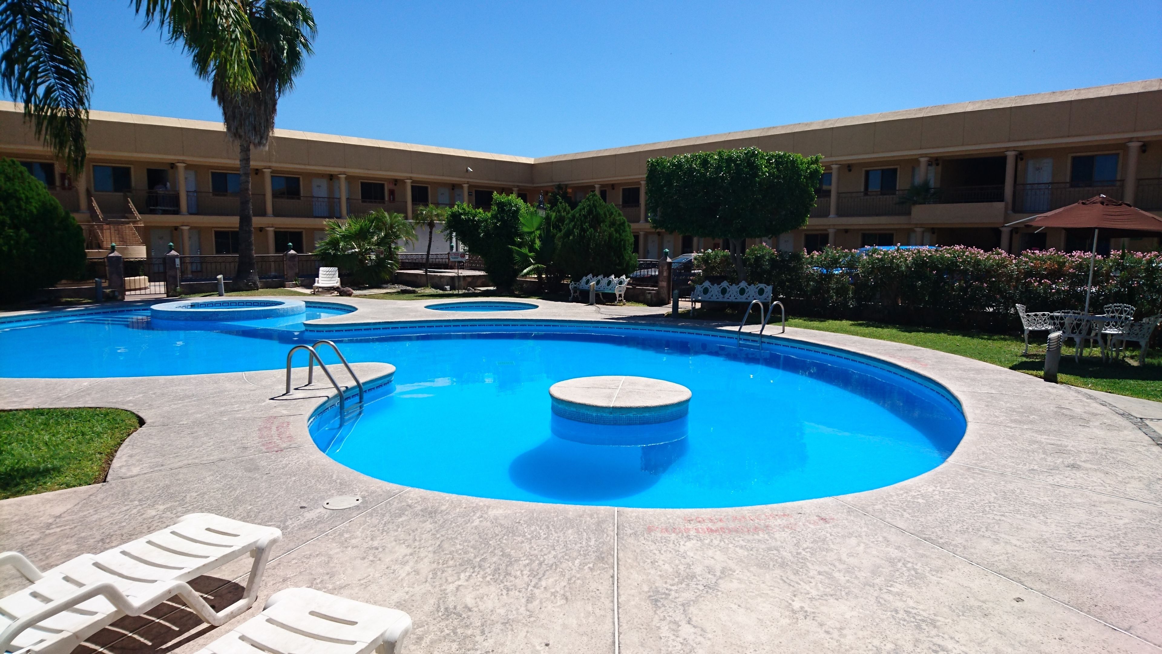 A swimming pool area with multiple pools, lounge chairs, and a building with balconies in the background.
