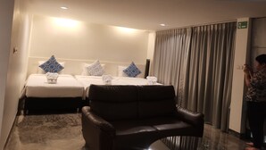 Een hotelkamer met twee bedden, een leren fauteuil en een groot raam met gordijnen.