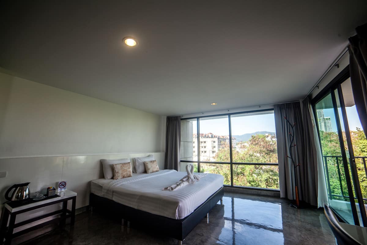 Une chambre d’hôtel moderne avec un grand lit, une table de chevet et une vue sur la ville grâce à de grandes fenêtres.