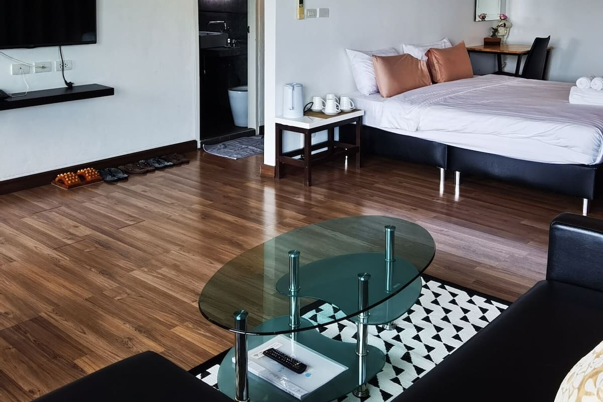 Une chambre d’hôtel moderne dotée d’une télévision à écran plat, d’un lit placé près d’une grande fenêtre, d’un coin repas avec une table en verre et d’un espace cuisine.