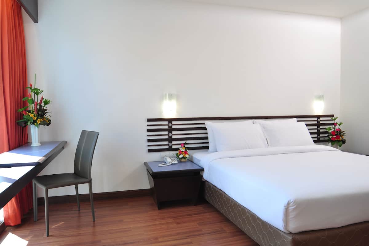 A hotel room with a bed, a desk, a chair, a nightstand, and two wall-mounted lamps.