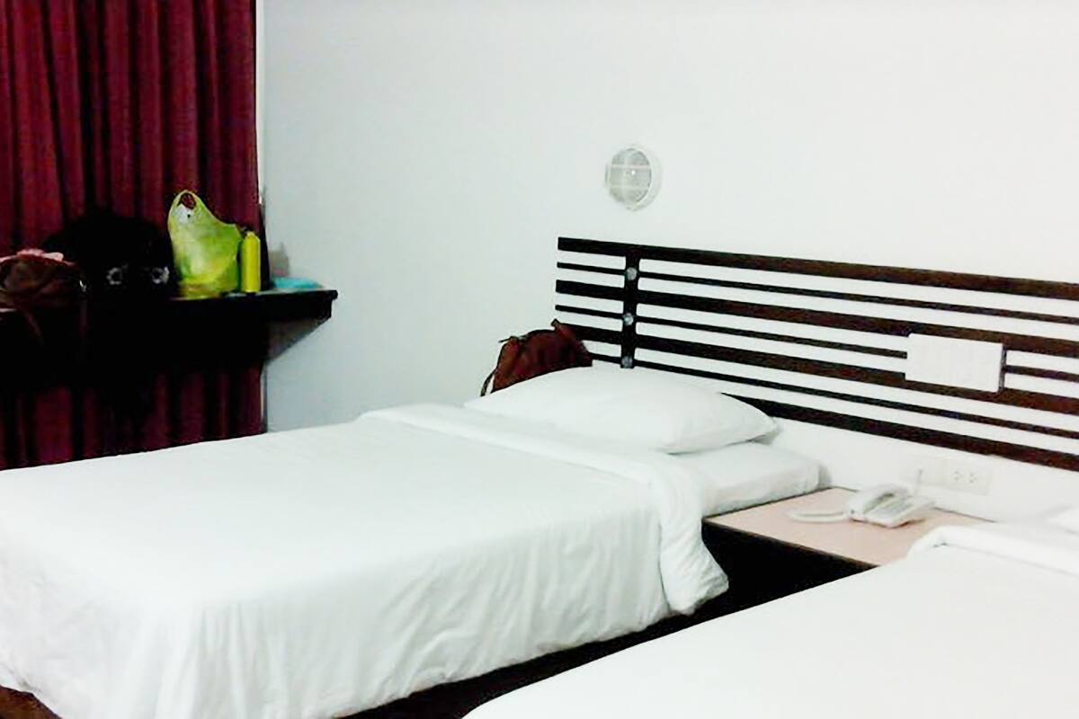 A hotel room with two single beds, a bedside table with a lamp, and a red curtain.