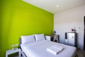 Habitación de hotel con cama, escritorio, refrigerador y una pared de acento verde.