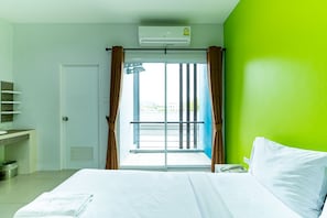 Une chambre d’hôtel avec un lit, une fenêtre avec des rideaux, une salle de bain avec une douche et un mur vert.