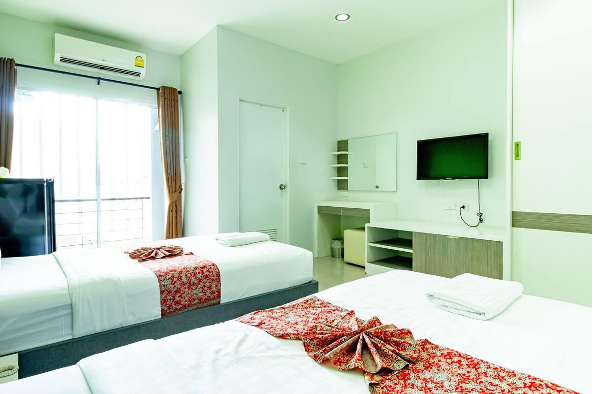 A hotel room with two beds, a TV, a desk, and a window with curtains.