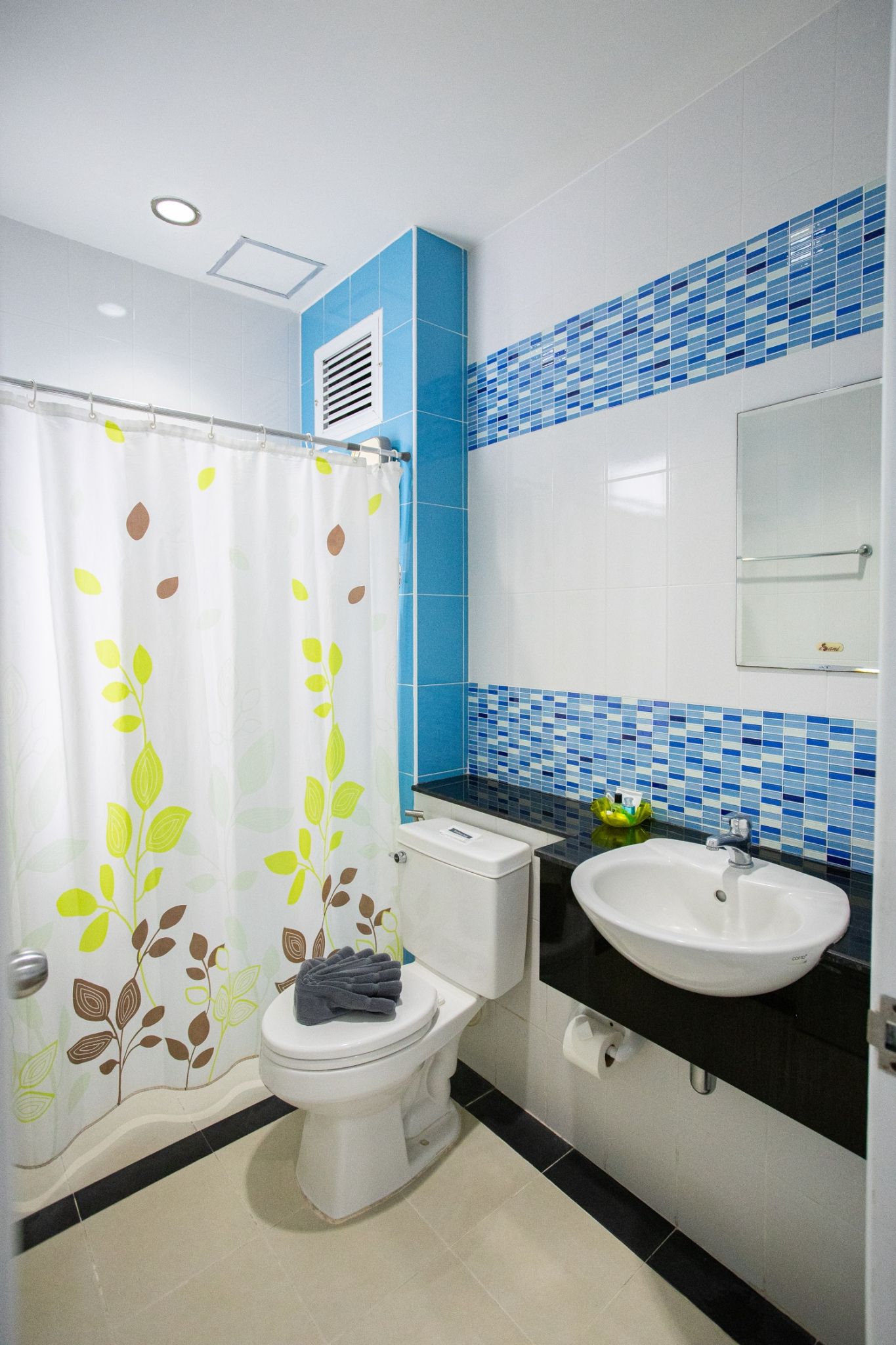 A bathroom with a toilet, a sink, and a shower curtain with leaf patterns.