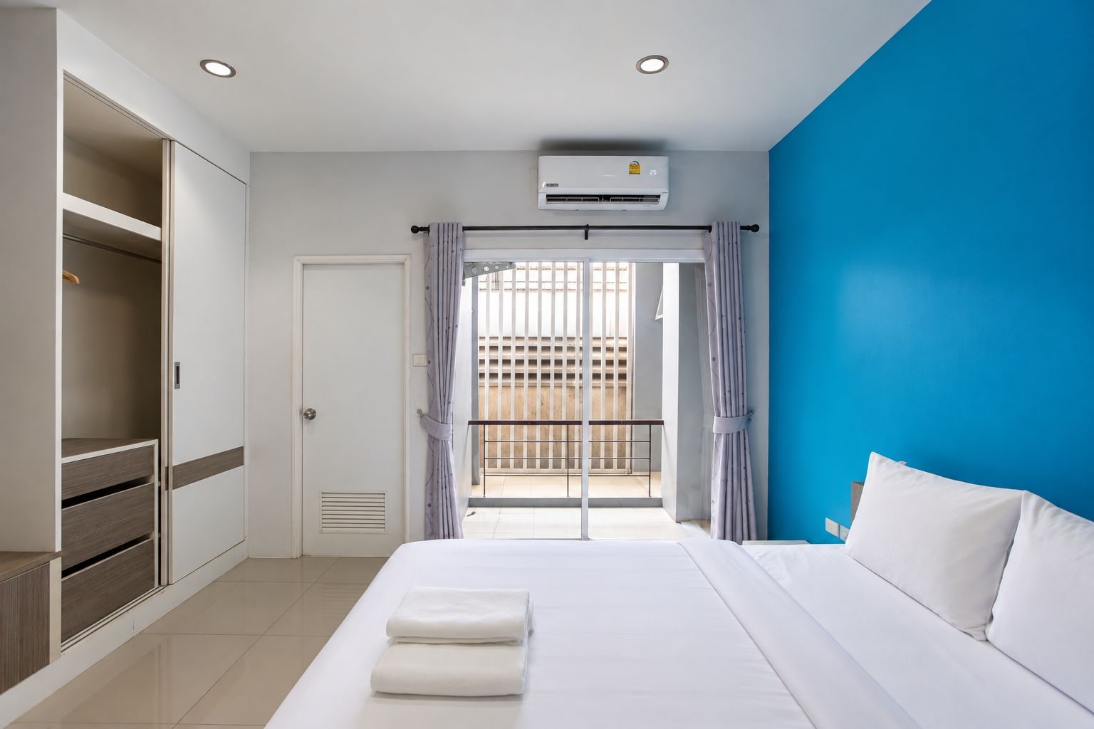 A hotel room with a bed, a wardrobe, a balcony with a view, and an air conditioning unit.
