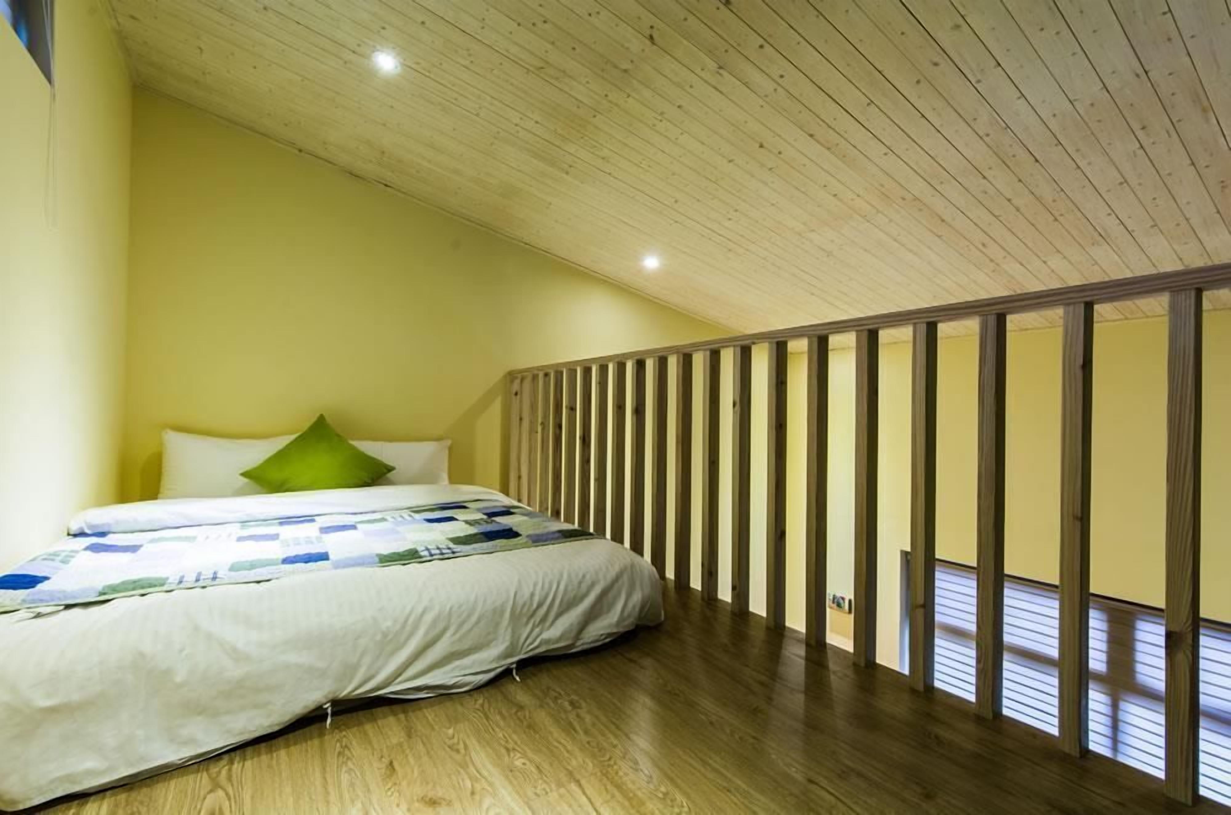 A bedroom with a wooden ceiling, a bed with a quilt, and a wooden partition wall.