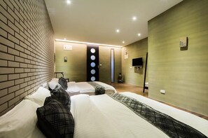 A hotel room with a brick accent wall, a large bed with patterned bedding, a flat-screen TV, and a wall-mounted circular light fixture. - LITHO Hostel (Hualien City)