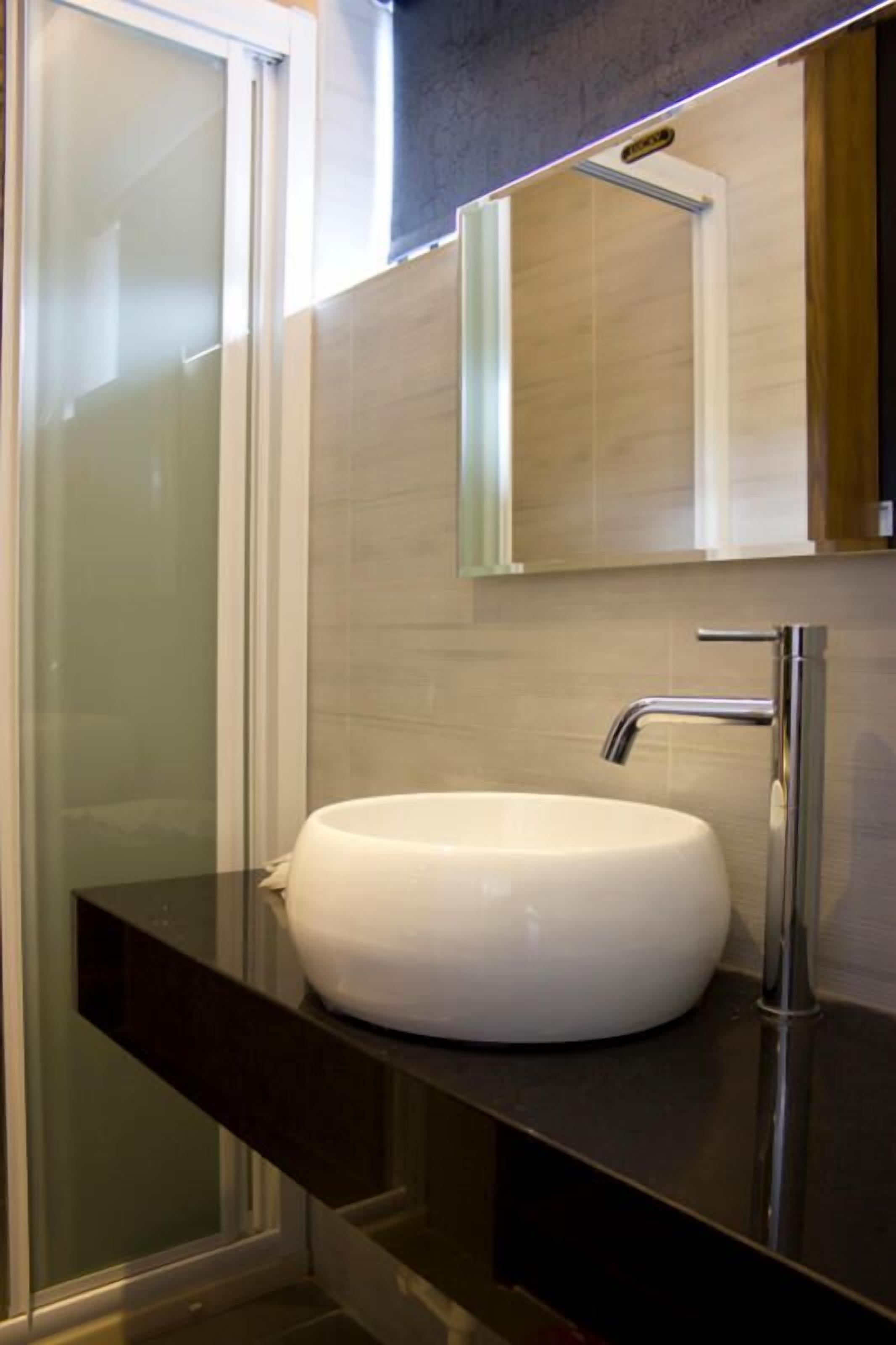 A modern bathroom with a white sink, chrome faucet, and a glass shower enclosure.