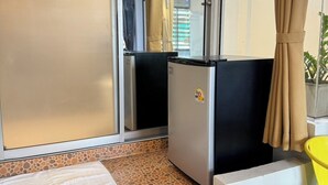 Una habitación compacta con refrigerador, una mesita, una silla y una ventana con cortinas.
