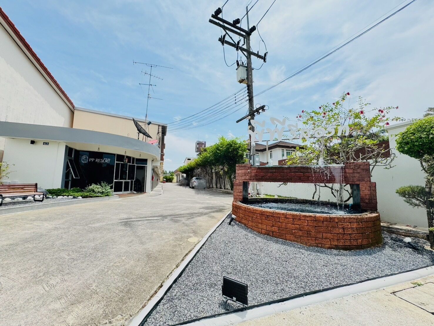 Vista de una calle con un edificio que dice "PP RESORT" y una pequeña fuente de ladrillo.