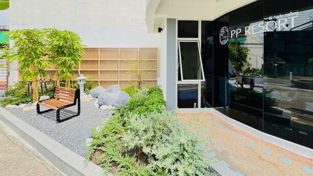 Un edificio moderno con fachada de vidrio, un banco de madera y un pequeño jardín con rocas y plantas.