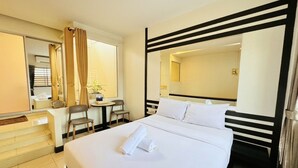 Habitación de hotel con una cama grande, un escritorio y una silla. Hay un espejo en la pared y una ventana con cortinas.