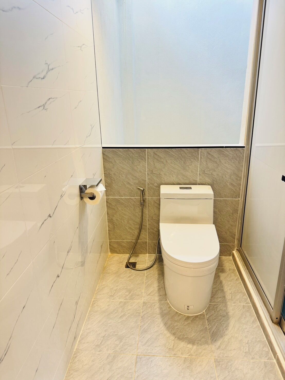 A bathroom with a toilet, a shower, and a toilet paper holder.