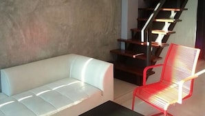 Uma sala de estar moderna com um sofá branco, uma poltrona vermelha e uma mesa preta. Há uma escada com degraus de madeira e um corrimão de metal.