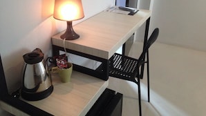 Quarto pequeno e compacto com escrivaninha de madeira, luminária, chaleira e uma cadeira.