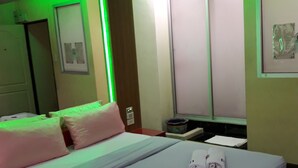 Habitación de hotel con cama, almohadas, mesita de noche, televisor y ventana con persianas.